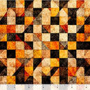 A close-up of wide quilt backing fabric with a checkerboard-like pattern featuring a geometric design of triangles and squares in black, orange, yellow, and beige, with a ruler visible along the bottom edge for scale.