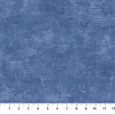 A close-up of a wide quilt backing flannel fabric swatch with a textured looking print in a denim blue, with a white ruler along the bottom edge showing measurement markings.